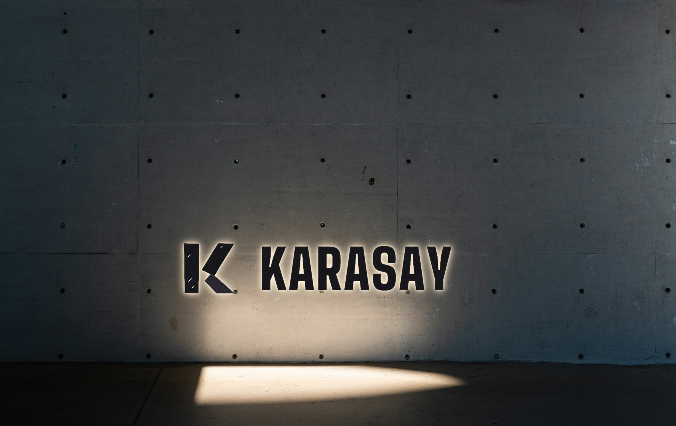 Spot ışığı altında koyu duvarda Karasay arkadan aydınlatmalı metal harfler konsepti